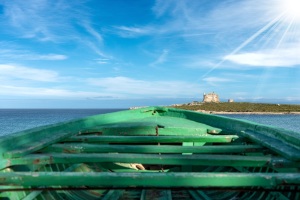 Green wooden boat of migrants and Mediterranean Sea in Portopalo di Capo Passero, Sicily island, Syracuse, Italy, south Europe